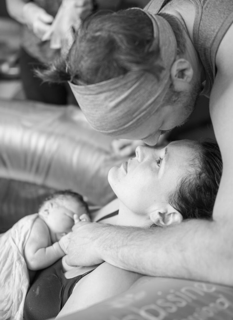 partner kisses birthing person in birthing pool black and white